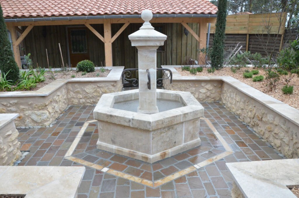 Fontaine en pierre au centre d’un jardin structuré